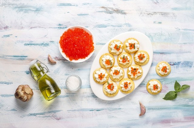 On a white marble table, a bowl with red caviar and a plate with caviar canapés.